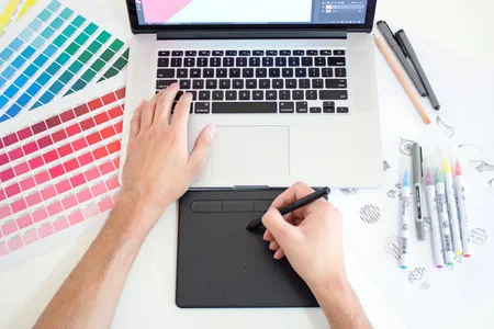 A designer drawing on a tablet beside color swatches